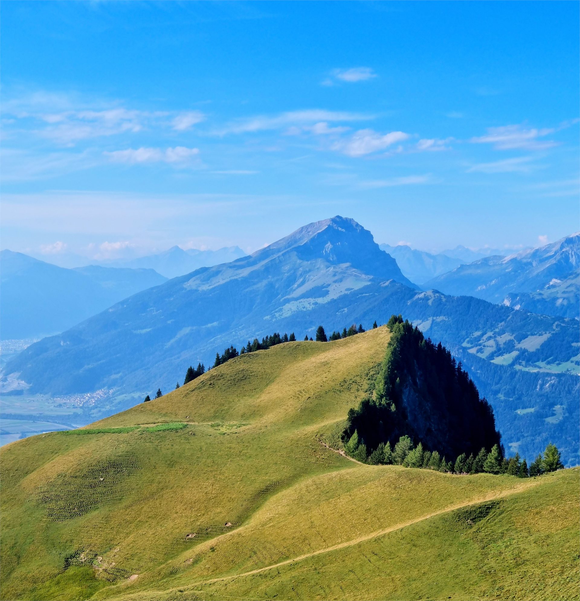 A sunny alpine ridge with Swiss mountains in the distance.