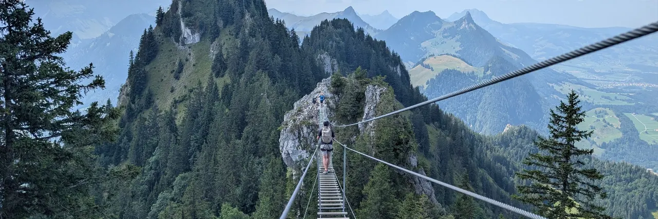 A via ferrata suspension bridge above a green mountain valley.